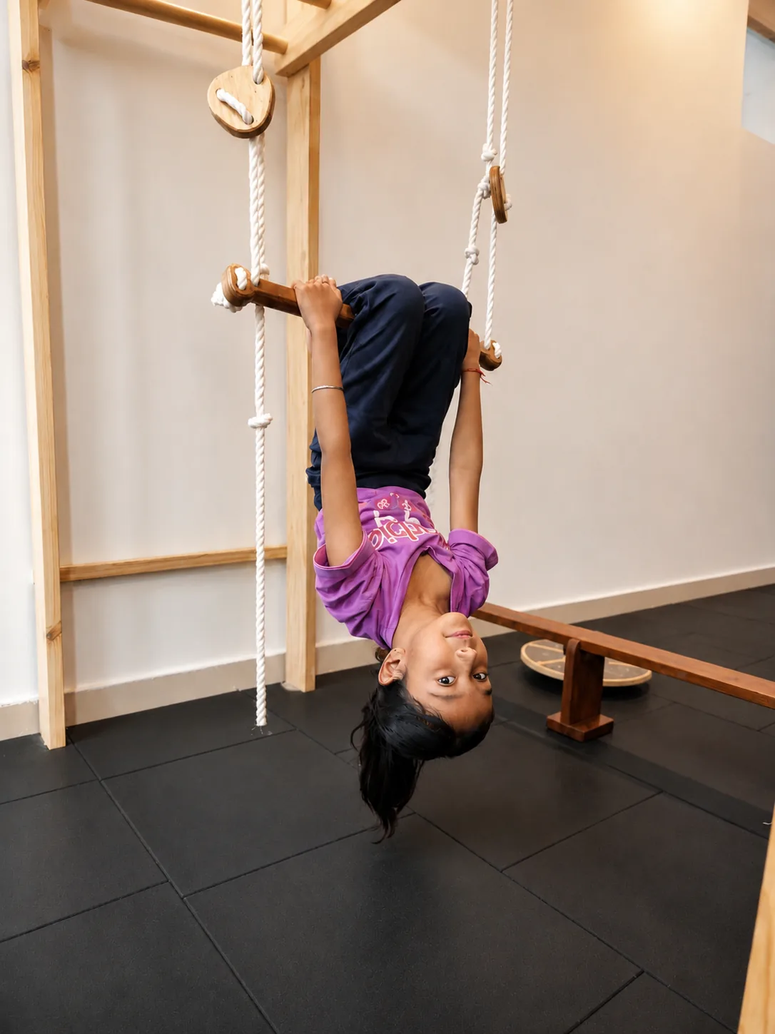 Child hanging upside down from Calineo Trapeze Bar on Playtower
